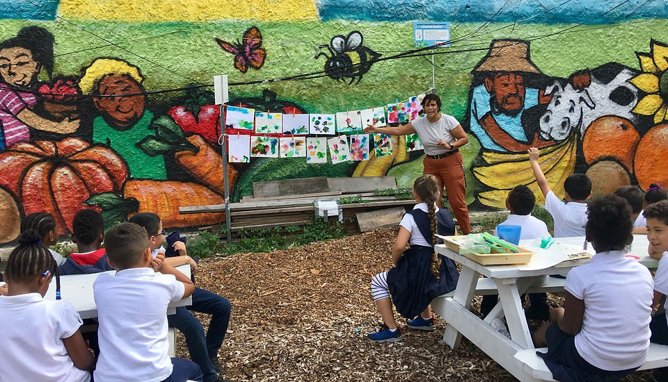 Students sitting at a picnic table giving feedback to their classmates' art work in the school garden.